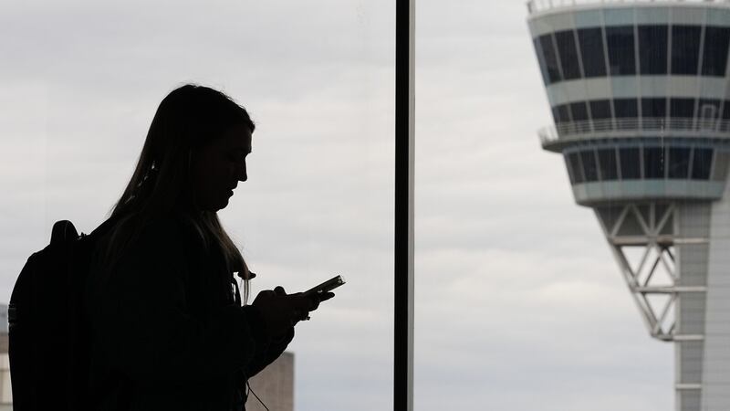 FILE - A traveler with a smartphone walks past an air traffic control tower at Philadelphia...